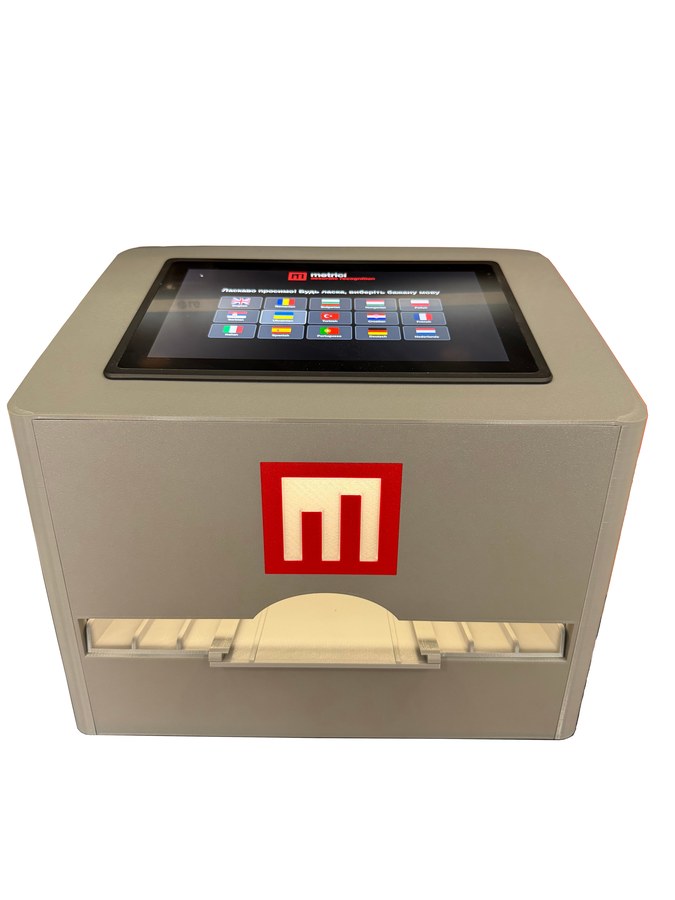 Metrici Document Scanner — grey desktop unit with a 10-inch touchscreen on top showing the language selection screen, the red Metrici logo on the front, and a document tray below.